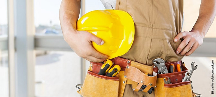 Handwerker mit gelbem Schutzhelm und Werkzeuggürtel, bereit für den Einsatz auf der Baustelle.