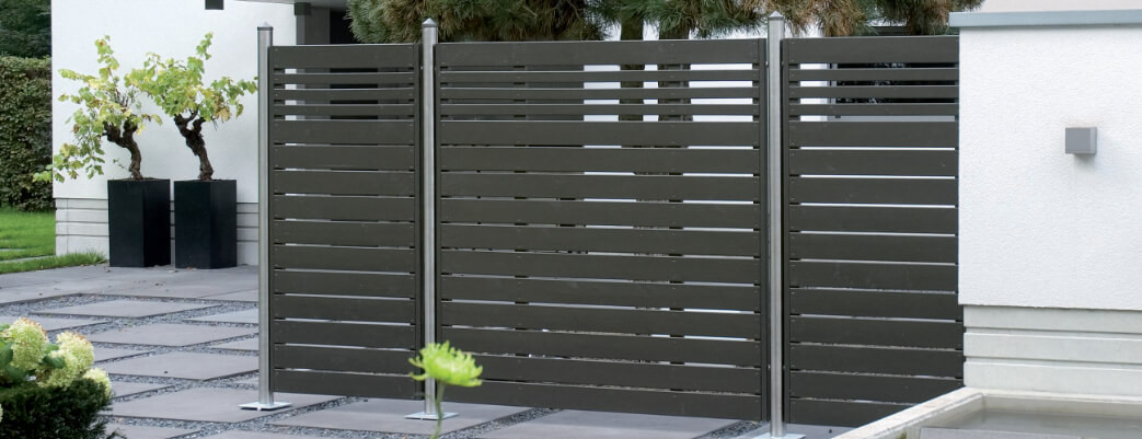 Moderner Garten mit grauem Sichtschutzzaun, gepflastertem Weg und bepflanzten Kübeln