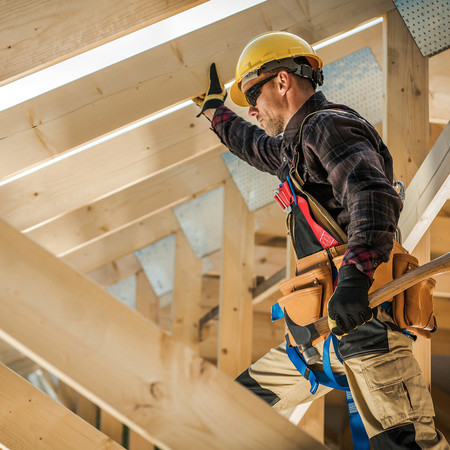 Zimmermann mit Schutzhelm und Werkzeug befestigt Konstruktionsvollholz (KVH) beim Bau eines Dachstuhls.