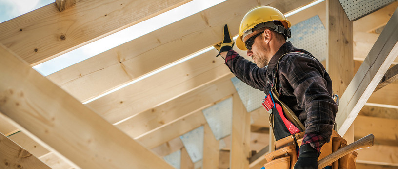 Zimmermann mit Schutzhelm und Werkzeug befestigt Konstruktionsvollholz (KVH) beim Bau eines Dachstuhls.