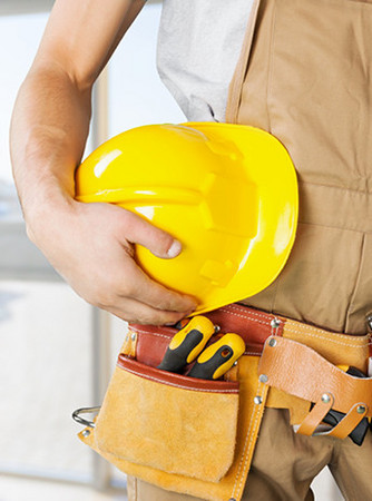 Handwerker mit gelbem Schutzhelm und Werkzeuggürtel, bereit für den Einsatz auf der Baustelle.